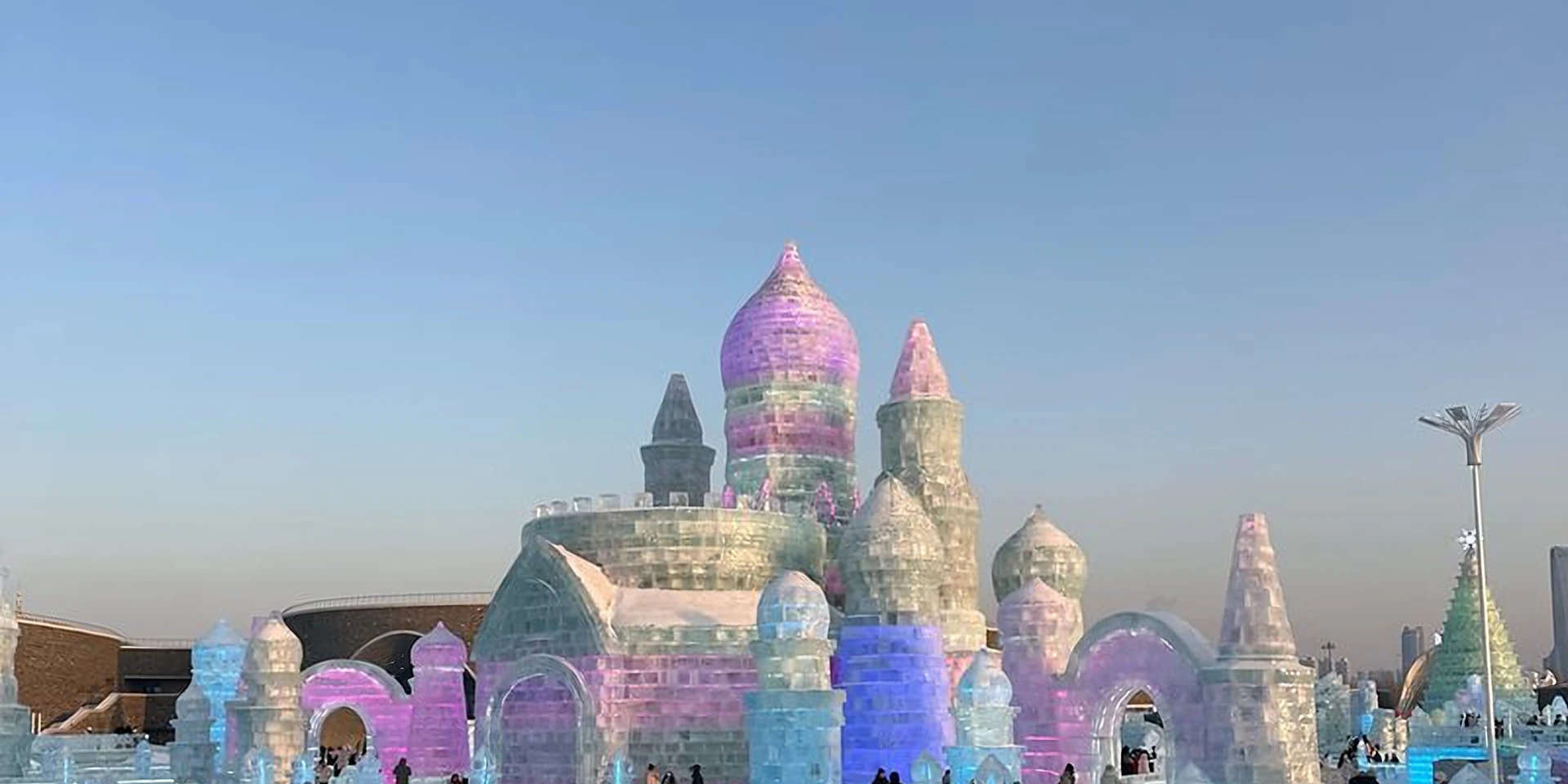 Daytime ice castle at Harbin Ice and Snow World with visitors walking a snow path toward the lit blue-and-white façade