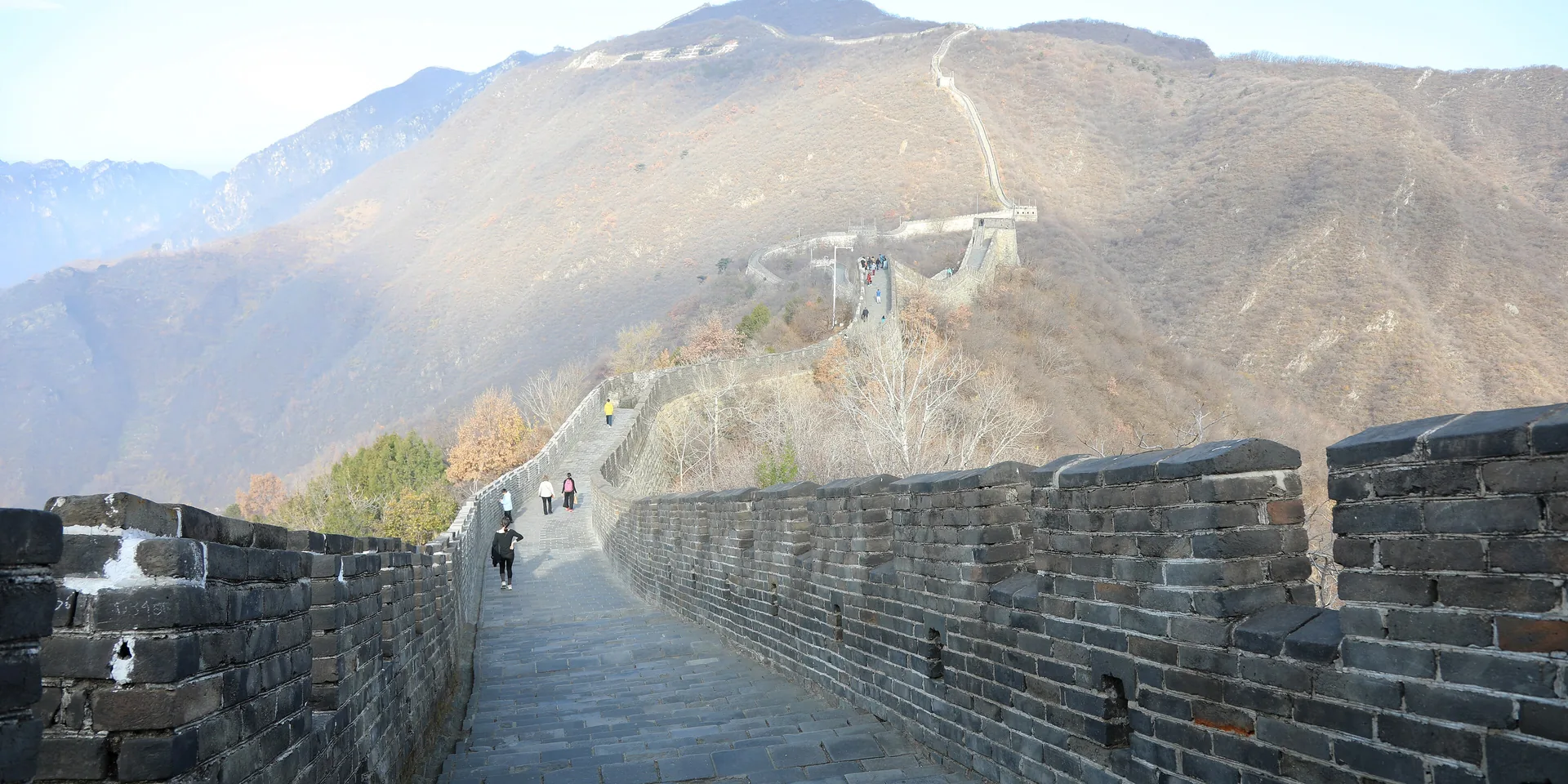 The Great Wall at Mutianyu running up a ridge of autumn-brown hills under a clear sky, stone walkway and battlements in the foreground
