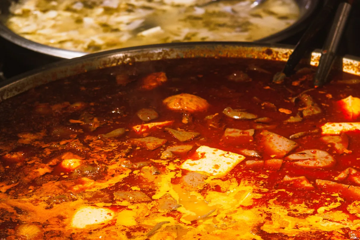 Bubbling red chilli hotpot broth with tofu beside a milder pot of broth