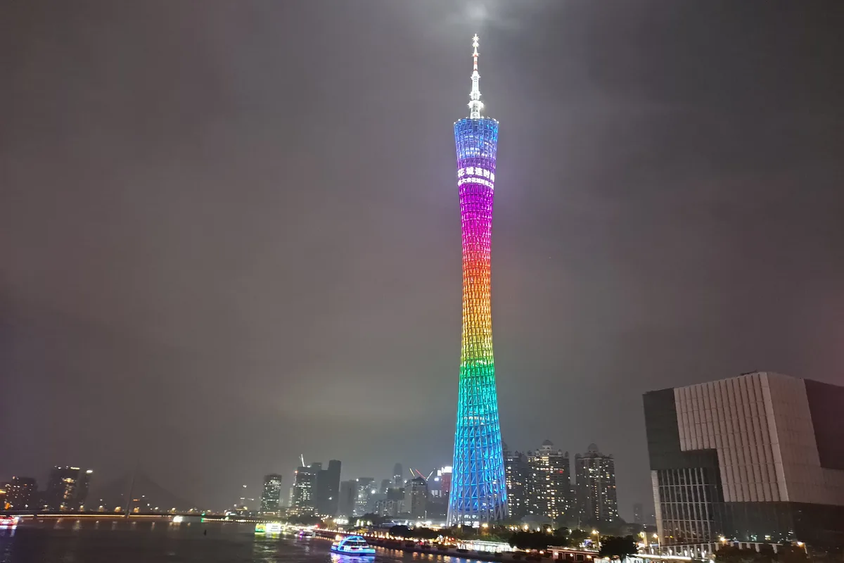 Canton Tower lit in rainbow colours above the Pearl River at night in Guangzhou, with tour boats and riverside buildings