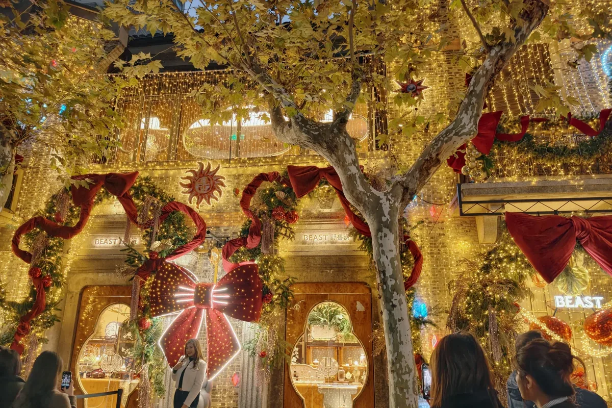 THE BEAST storefront in a Shanghai Shikumen lane wrapped in golden string lights, giant red bows, and Christmas greenery—crowds photographing the display