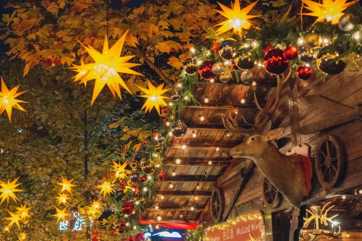 Glühwein / 热红酒 stall at a Shanghai Christmas market—wooden cabin, Moravian star lights, winter crowd with mulled-wine cups