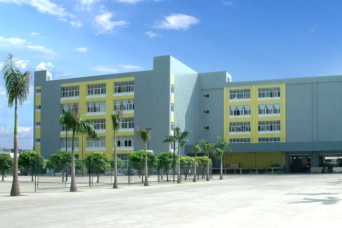 A five-storey grey and yellow furniture factory building with palm trees and a large paved yard in front, in Shunde, Foshan, under a blue sky