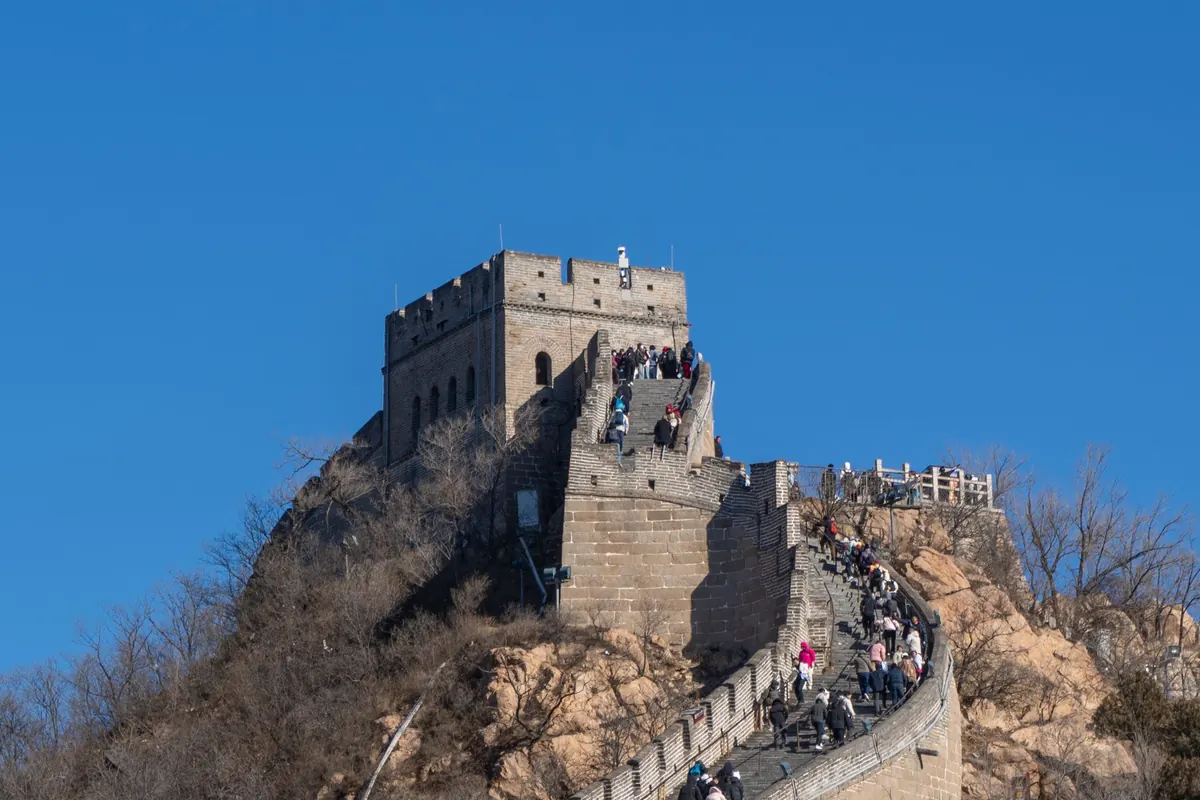 Crowds climbing a steep stair on the Great Wall of China toward a watchtower under a clear blue sky