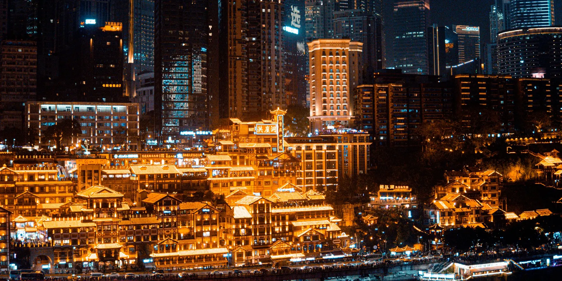 Hongyadong in Chongqing lit gold at night, stilted riverside buildings below the illuminated towers of Yuzhong